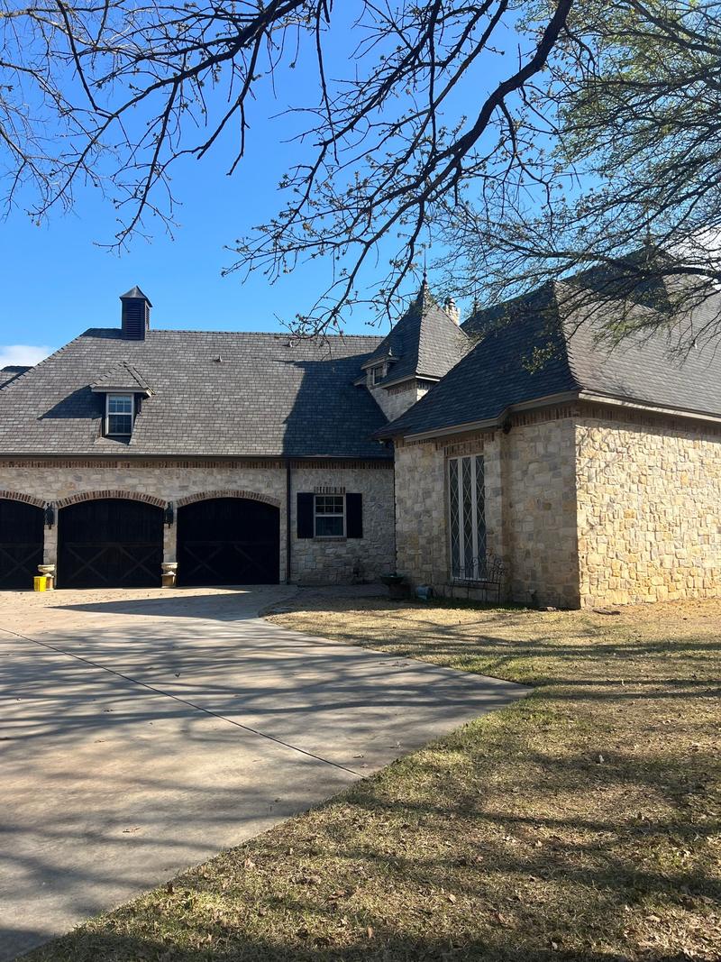 Full front view of a slate-look shingle roof on a stone French-country home near Bridgeport, TX