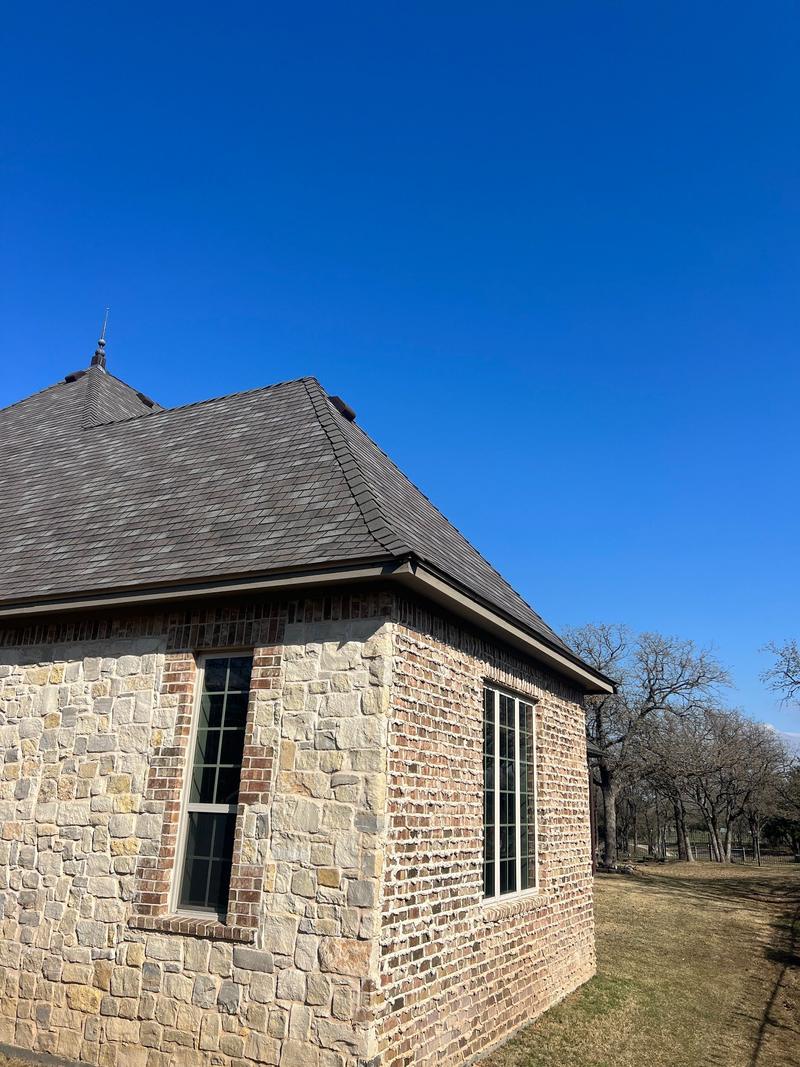 Steep hip roof in multi-tone slate-look shingles on a stone and brick home