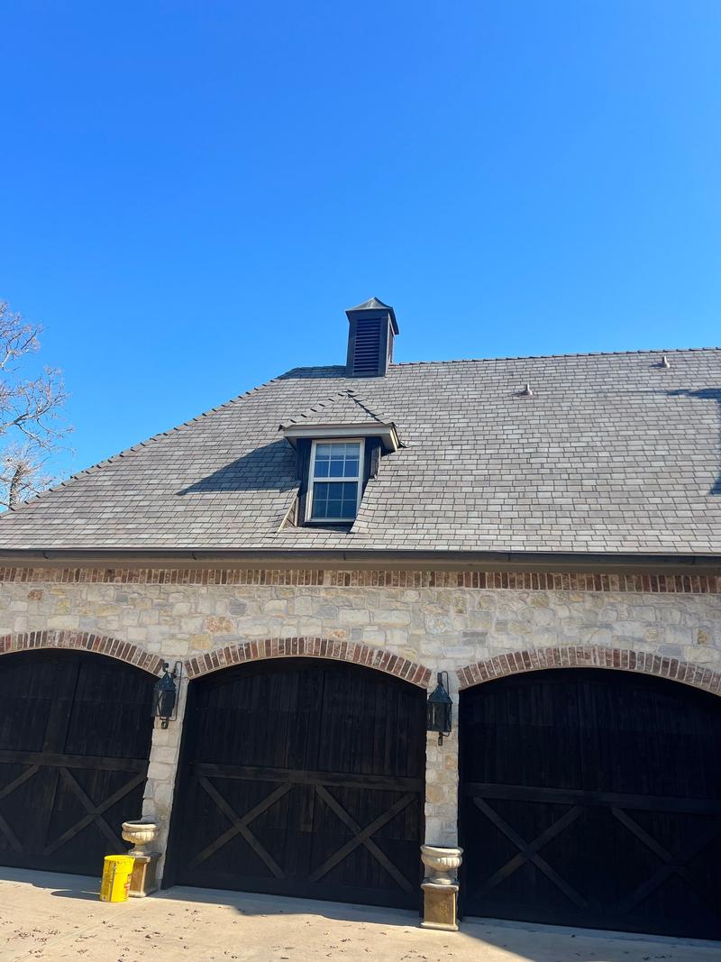 Slate-look shingle roof over arched garage bays on a stone home