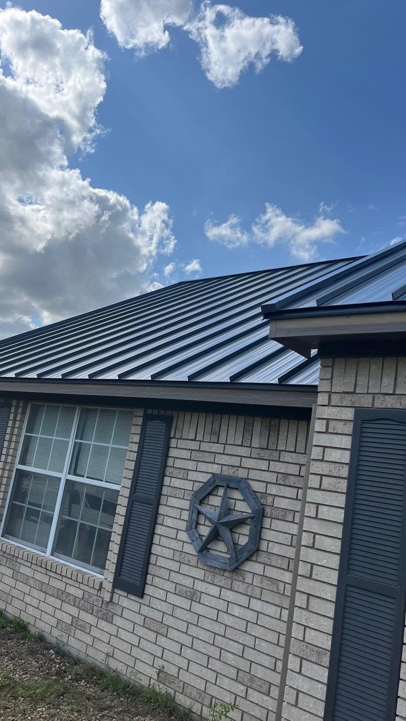 Charcoal standing seam metal roof on a brick home with dark shutters