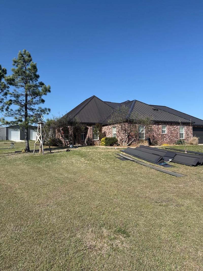 Red brick ranch home with a new dark standing seam metal roof, seen from the front yard