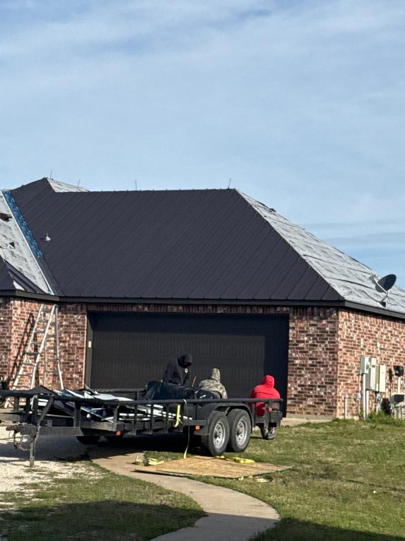 Snow Roofing crew at the panel trailer beside a brick garage during a standing seam install
