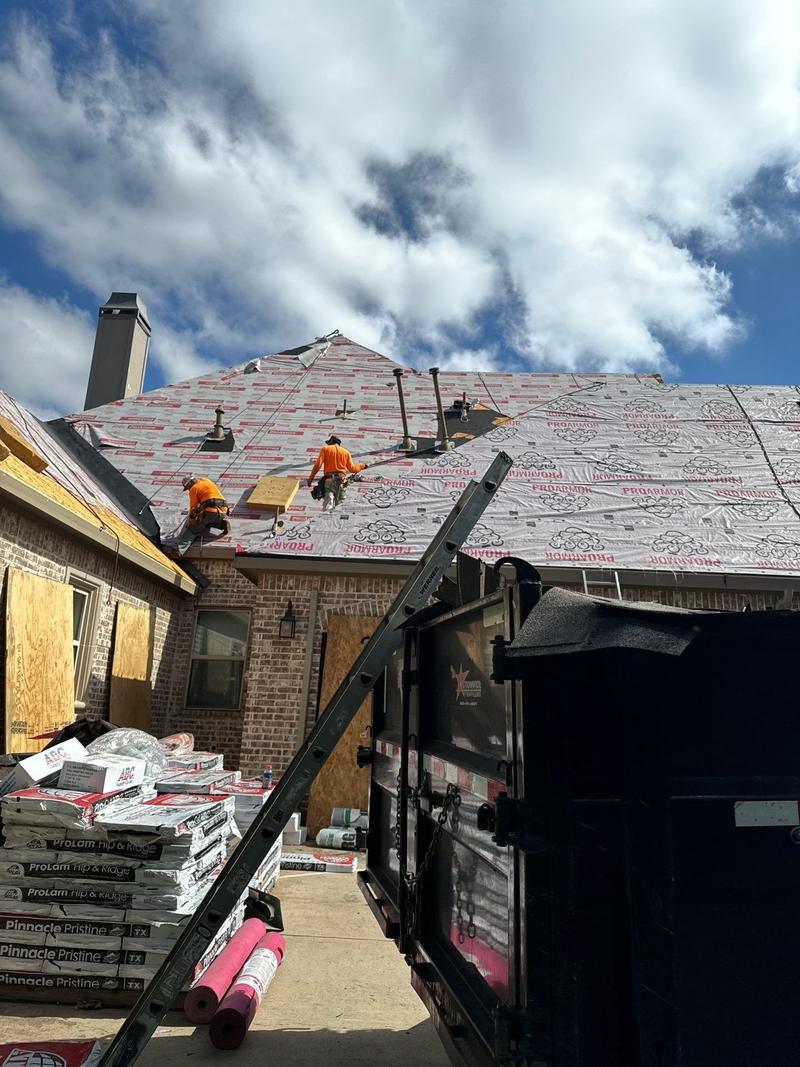 Roofing crew on synthetic underlayment with roofing materials staged below